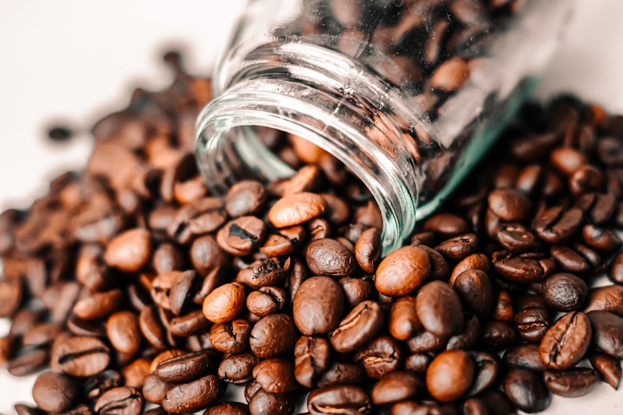 our-services-3 A detailed shot of aromatic coffee beans spilling from a transparent glass jar onto a surface.