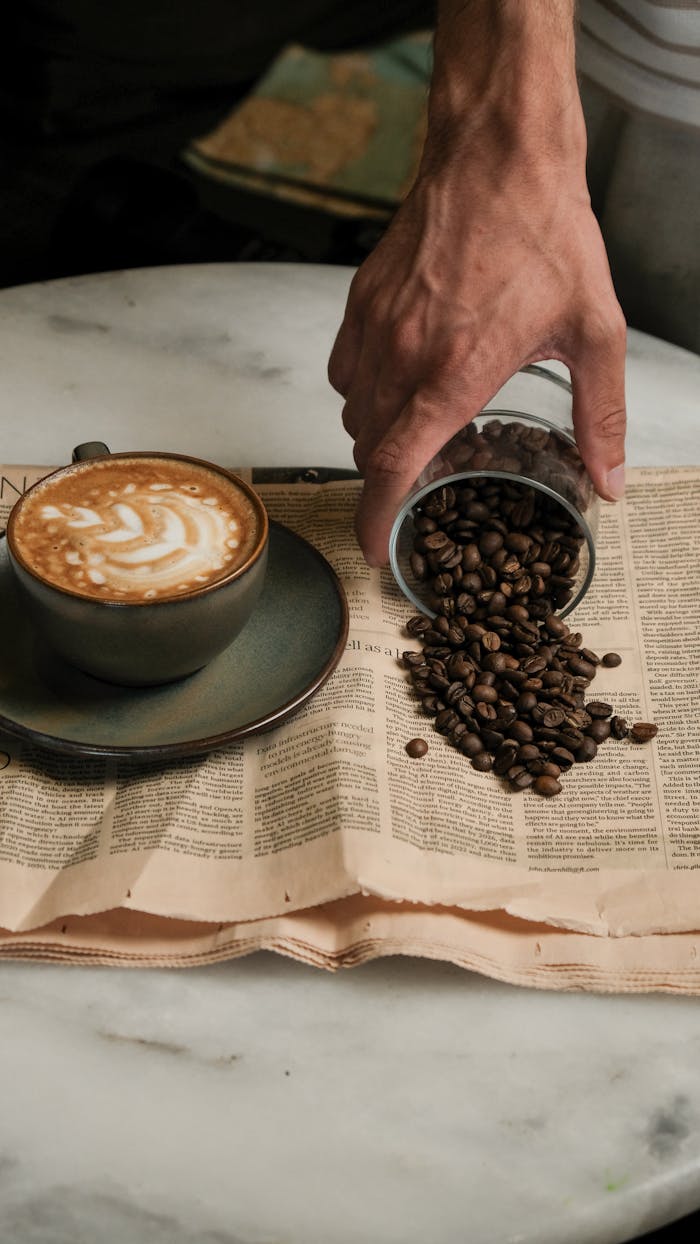gallery-5 Artistic composition of cappuccino and spilling coffee beans on a newspaper.