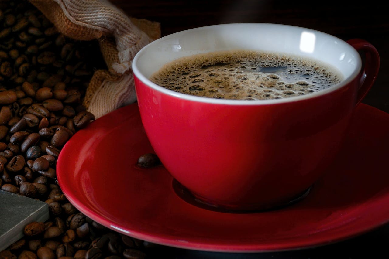 contact-img A steaming cup of espresso in a red mug surrounded by coffee beans. Perfect for morning routines.