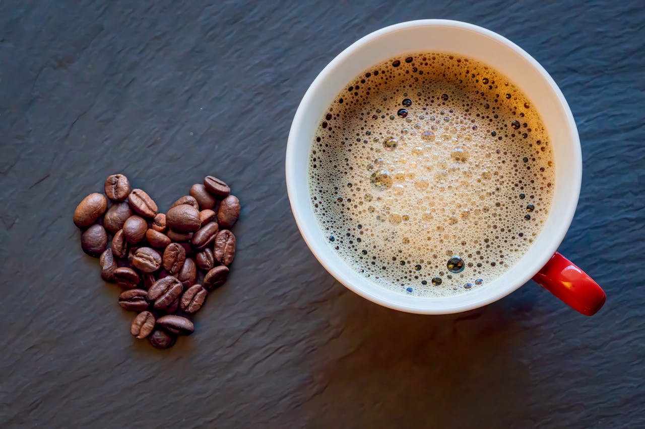 gallery-6 A red cup of coffee and heart-shaped coffee beans on a dark surface.