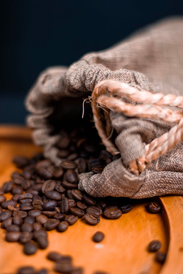 gallery-4 A burlap sack pours aromatic roasted coffee beans onto a wooden tray, highlighting texture and richness.