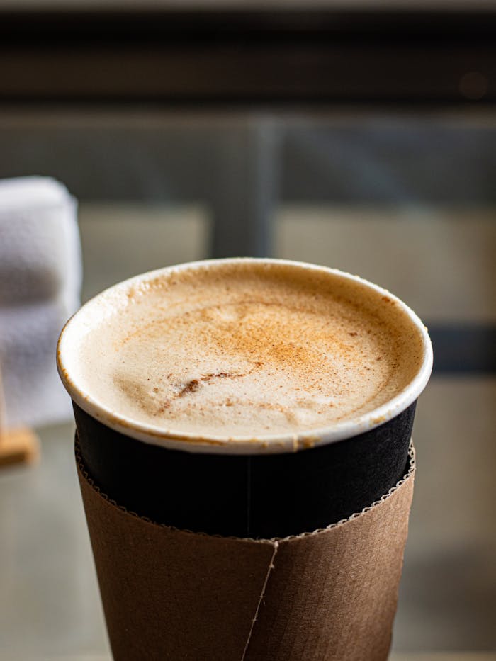 gallery-1 Close-up of a cinnamon-spiced chai latte with foam in a disposable cup, perfect for cozy moments.