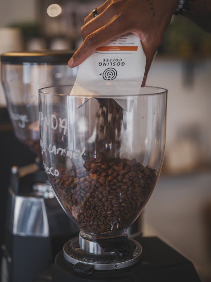 our-experience Hand pouring premium coffee beans into grinder in a cafe setting.
