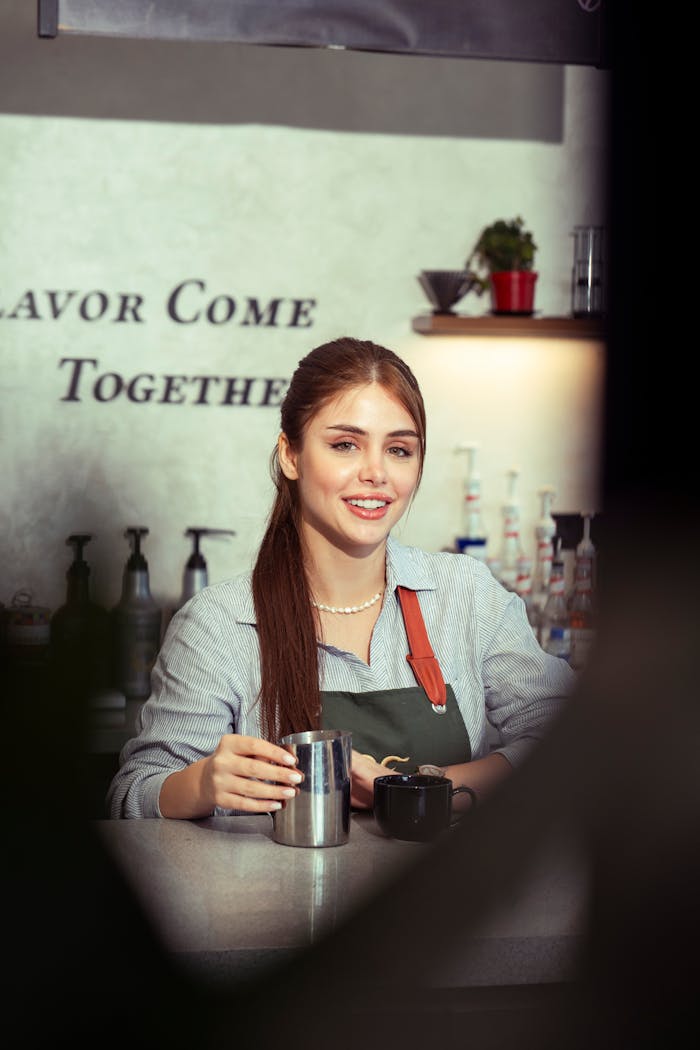 hero-img-01 Young female barista smiling while preparing coffee in a cozy cafe setting.