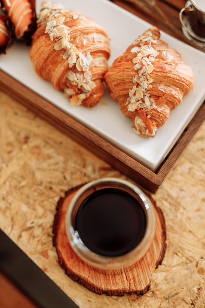 our-services-1 Fresh almond croissants served with coffee on a rustic wooden table.